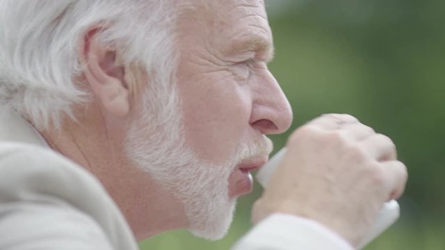 Senior man laughs during a conversation and takes a sip of his drink