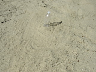 A mostly empty plastic water bottle sitting in the sand and casting a shadow 