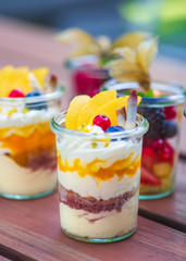 Dessert Nachspeise im Glas mit Crumble, Creme, Früchten, Mango, Biskuit au feinem Holztisch serviert auf einer Party vom Catering. schön angerichtet