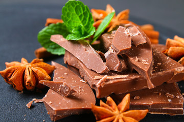 Pieces of chocolate, cinnamon and star anise on a dark grey table.