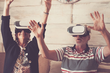 couple of senior adult caucasian enjoy technology with goggled headset and play in virtual realuty together having fun at home. trying new experience together for life