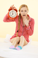 Shocked woman wearing pajamas holding clock