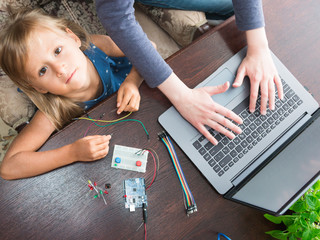 A cute girl with a teacher collect robot arduino and program it on the computer. The boards and microcontrollers are on the table. STEM education. Programming. Mathematics. The science. Technologie.