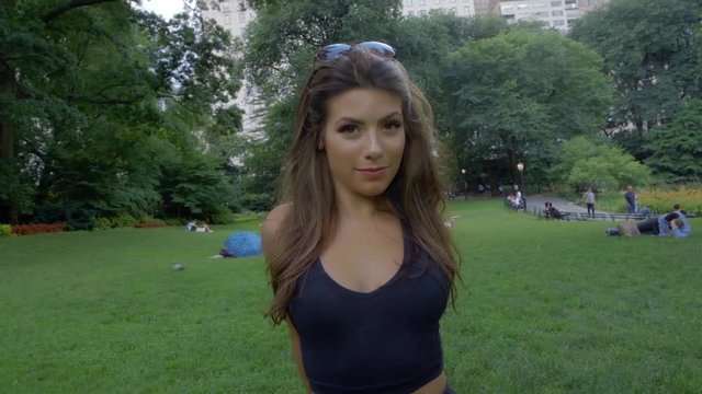 Young Caucasian Woman With Long Brunette Hair Standing On Grass In Park, Stretches And Warms Up Before She Begins Her Run