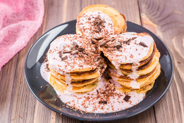 A pile of pancakes stuffed with fruit yoghurt and sprinkled with grated chocolate on a plate on a wooden table