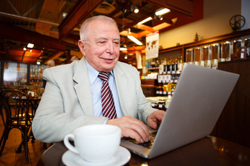 Fototapeta na wymiar business, technology and people concept - old senior businessman in suit and tie with laptop computer drinking coffee in city cafe