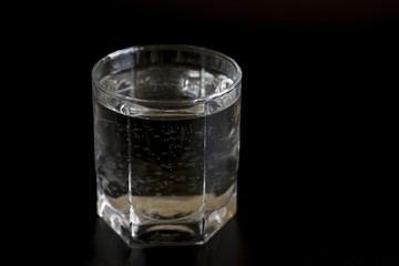 Glass with clear water on a black background.