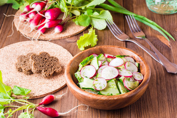 Lenten spring vegetable salad from cucumber, radish, greens and oil in a wooden plate