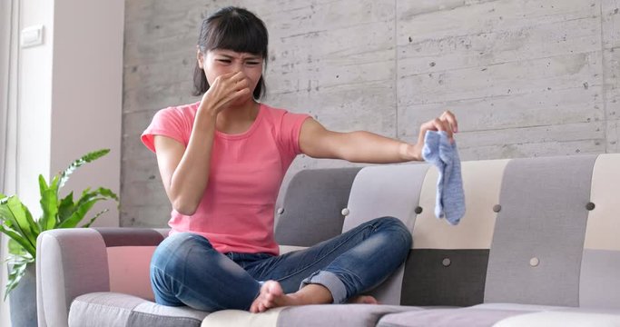 Woman holding smelly sock at home