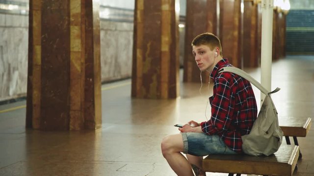 Young Man Using Smartphone Waiting for Subway Train at Metro Station