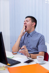Naklejka premium Young businessman yawing at workplace