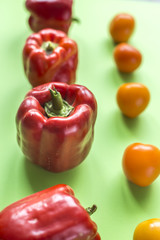 Red large pepper and yellow tomato. Bright photo on a green background