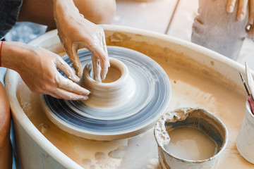 Top view of hands with clay making of a ceramic pot on the pottery wheel, hobby and leisure with...
