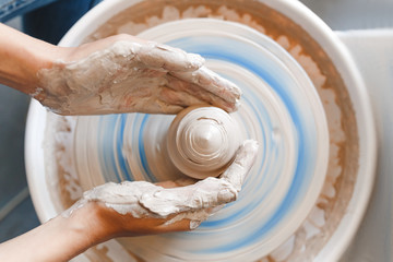 Top view of hands with clay making of a ceramic pot on the pottery wheel, hobby and leisure with pleasure concept - obrazy, fototapety, plakaty