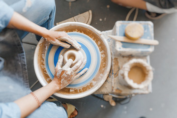 Top view of hands with clay making of a ceramic pot on the pottery wheel, hobby and leisure with...