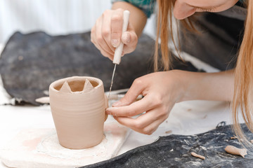 Close-up view of a female potter making and molding clay dishware in a workshop using different tools