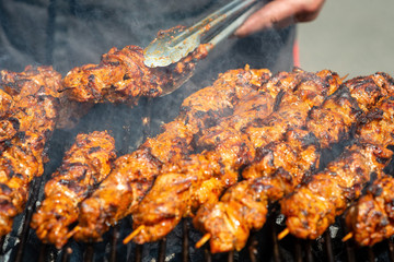 Meat on skewers fried on the grill in the open air, visible hands of the cook.