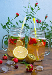 mug with homemade lemonade lemon and mint strawberries, kiwi on a wooden table laid out pieces of ice and fruit blurred blue background in the garden