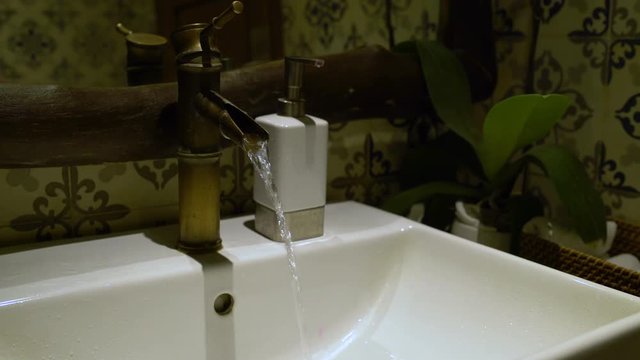 A man's hand opens a tap with water in the sink