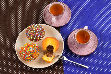 Baking with tea and chocolate on the table.  Two cups of tea with cupcakes and chocolate with a multicolored powder on the table.