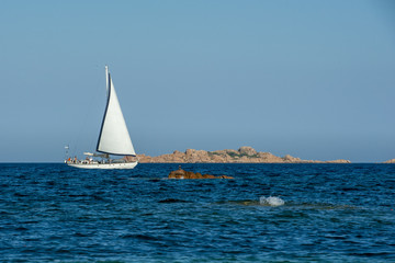 Obraz premium On a sunny summer day a white sailboat sails on Mediterranean Sea in Sardinia, luxury vacations.