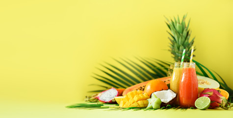 Juicy papaya and pineapple, mango, orange fruit smoothie in two jars on yellow background. Banner. Detox, summer diet food, vegan concept. Copy space. Fresh juice in glass bottles over palm leaves.