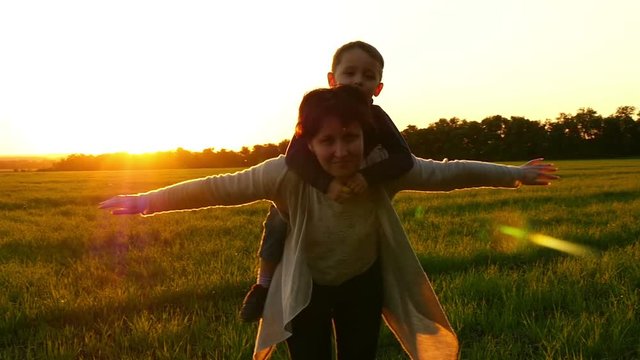 Mom and the child showing the flight of an airplane with their hands against the sunset. Beautiful family mom and boy. Mom keeps the baby on her back. Happy parent and child
