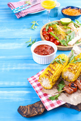 Grilled vegetables on a wooden plate and sausages, juice and salad on a blue background. Summer dinner. Free space for text. Copy space.