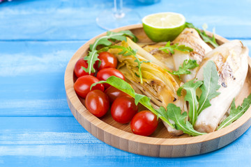 Vegetables grilled on a wooden plate and juice, on a blue background. Summer dinner. Free space for text. Copy space.