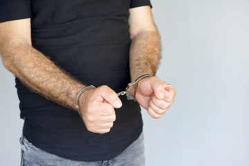 Close-up. Arrested man handcuffed hands isolated on gray background. Prisoner or arrested terrorist, close-up of hands in handcuffs.