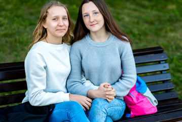 Two teenage girls. Summer on a bench in city after school. Happy resting holding each other's hands. The concept is best friends. Emotions and smiling happily.