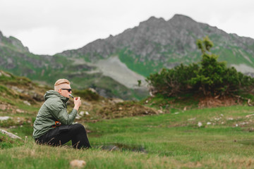 Mann wandert durch die Berge, sitzt und raucht Pfeife