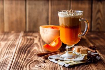 Pumpkin spice latte with whipped cream and cinnamon in glass on rustic wooden background