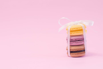 three macarons stack and tied together with white bow. on pink background.