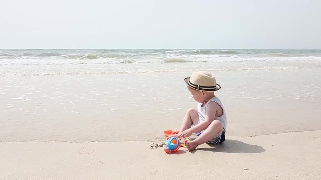 Little child playing in sand at the sea beach with toys. Happy kid boy having fun with sandy toys while his family relax at summer vacation