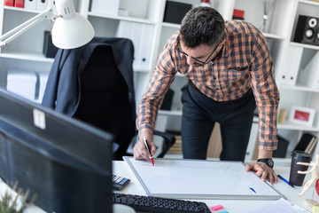 A man in the office is standing near the table and draws a marker on the magnetic board.