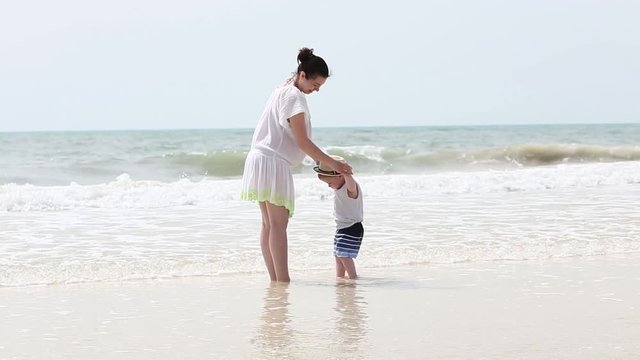 Happy hugs of beautiful mother and her toddler son outdoors at the sea beach. Young mum embrace her child boy at summer vacation on white sand. Happy family