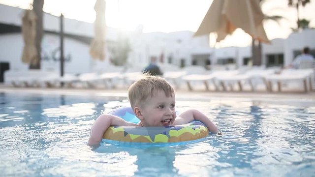 Little child boy swimming and playing in a open pool with happy smile. 3 years old kid swim in a circle in the pool for the first time at summer vacation