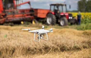 Drone in front of tractor and combine harvester in field
