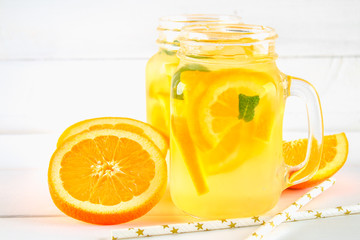 Orange detox water in mason jars on a white wooden table. Healthy food, drinks.