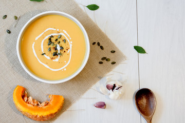 Pumpkin soup with pumpkin seeds. In white bowl, on hessian fabric. With rustic spoon and garlic. 
