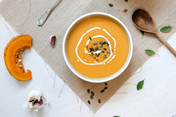 Pumpkin soup with pumpkin seeds. In white bowl, on hessian fabric. With pumpkin slice, rustic spoon and garlic. 