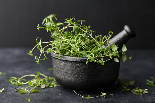 Fresh green thyme herb in cast iron spice grinder or mortar on black stone background, close up view
