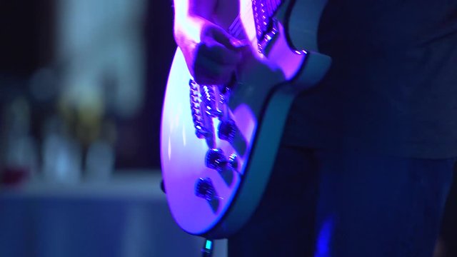 A teen or young adult plays an electric guitar in flashing colored lights