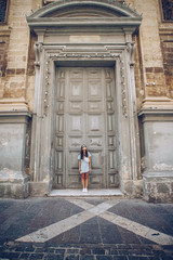 Portrait of beautiful tourist brunette woman in blue dress standing near the big old doors on the entrance of the catholic church.