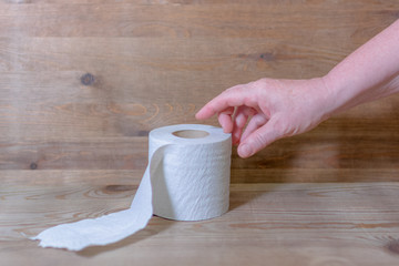 Hand reaches for toilet roll on wooden background
