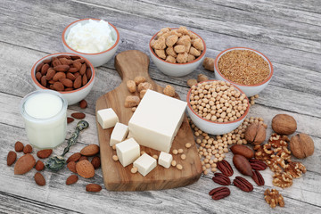 Health food for vegans with tofu, soy beans, nuts, seeds, soya yoghurt, milk and chunks,  Foods high in fibre, antioxidants, vitamins and minerals, on rustic wood  background.