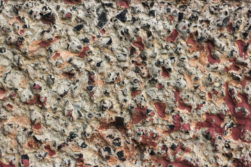 Ancient gray concrete wall with black interspersing stones and red dye. Granite stone stocco accidented background, city building wallpaper