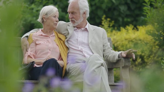 Romantic older couple talk on bench in a beautiful garden