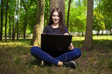 girl with a laptop sitting near a tree.
